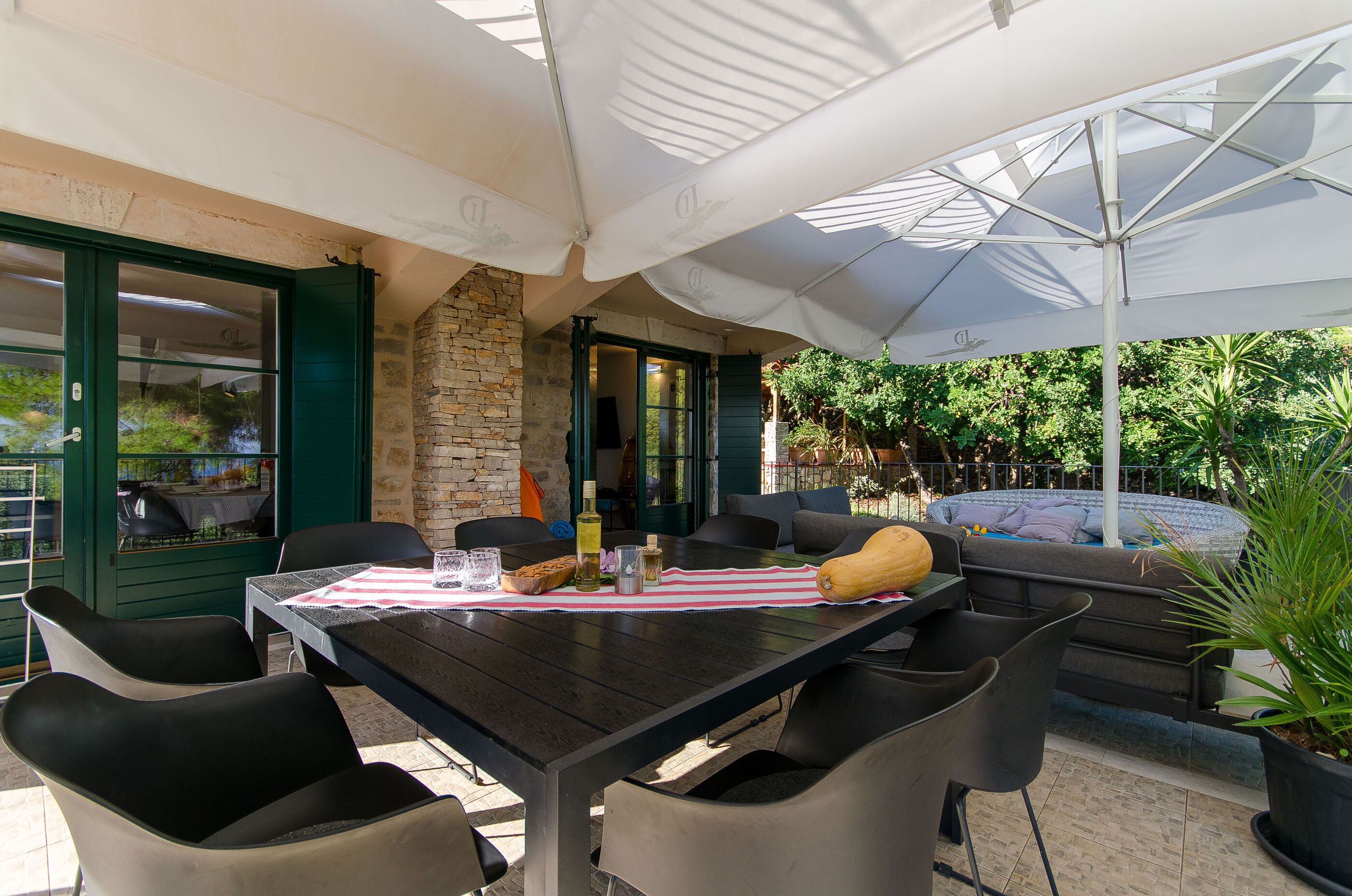 An outdoor patio with a table set for dining, surrounded by chairs, and an umbrella providing shade.