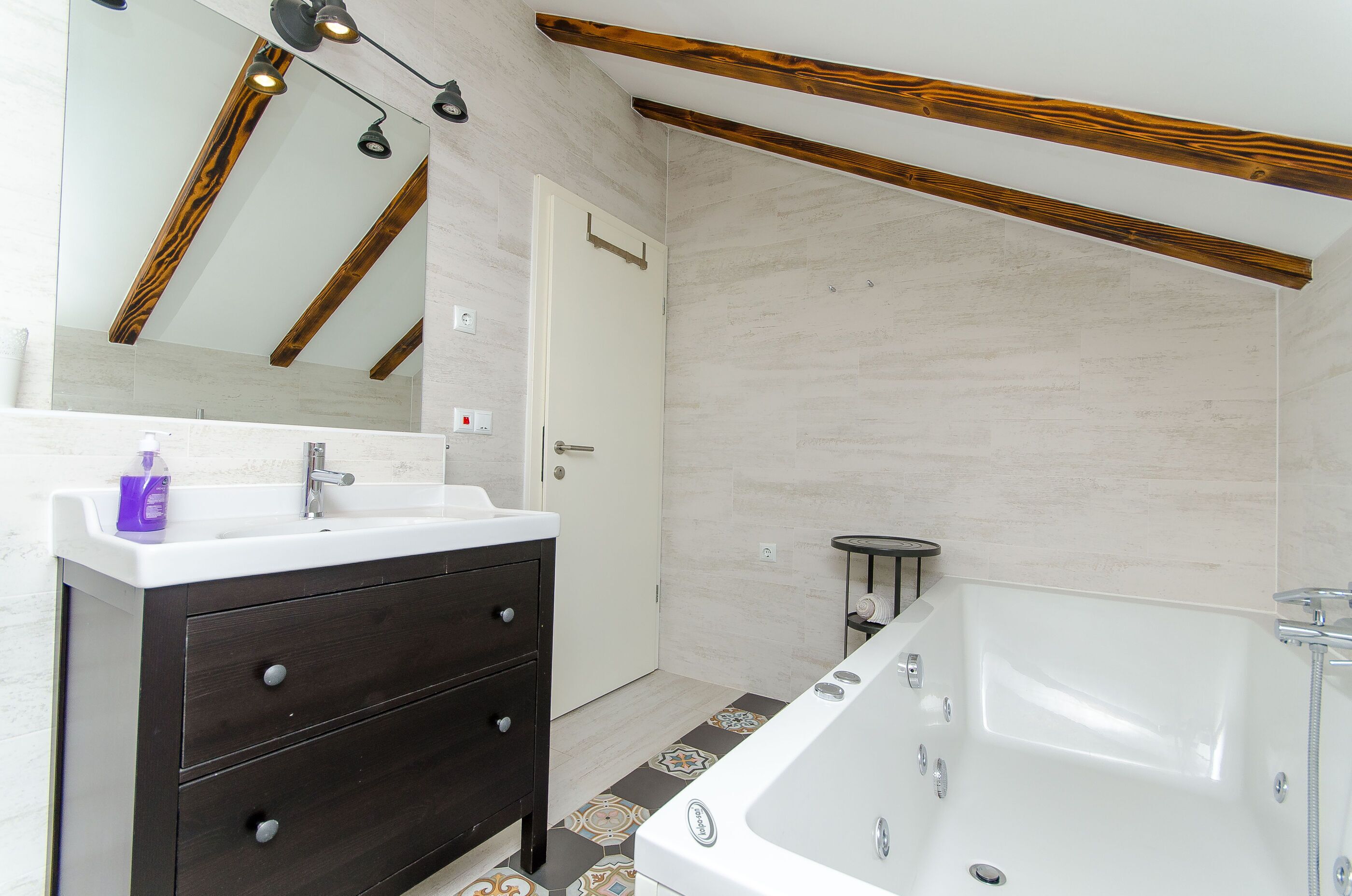 Un baño con una bañera blanca, tocador de madera oscura y un espejo con vigas de madera.