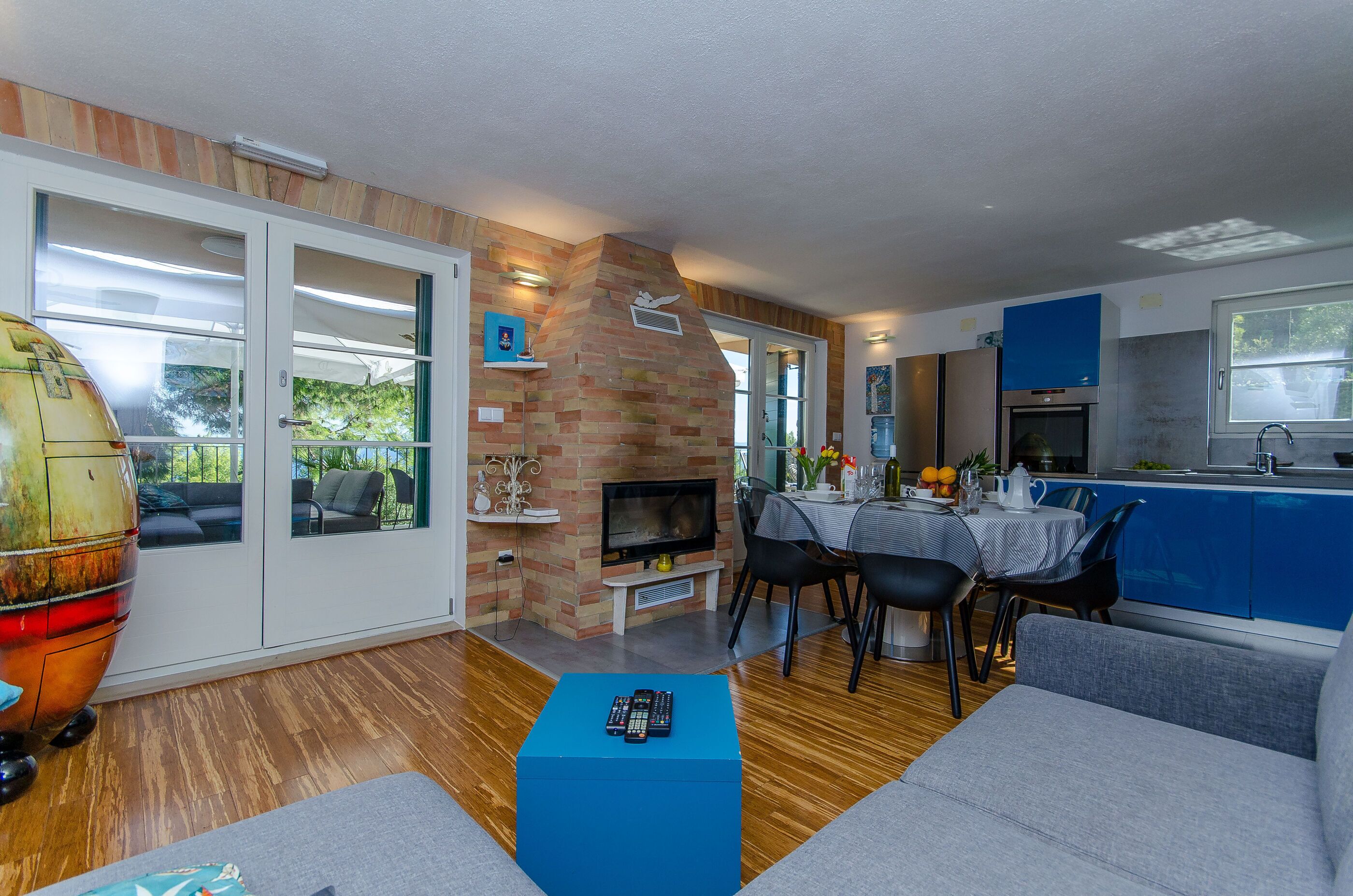 A modern living room with a fireplace, a dining area, and a kitchen with blue cabinets.