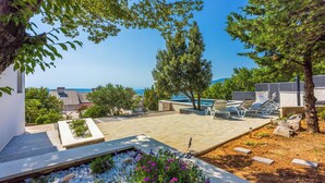 A patio with a view of the sea, outdoor seating, and a garden with flowers. - Villa Turquoise Breeze (Novi Vinodolski)