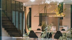 A modern interior with a staircase, a dining area with black chairs, and a kitchen with a hanging light fixture. - Villa Chic (Vodice)