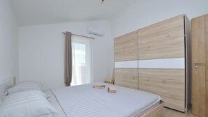 A bedroom with a bed, a wooden wardrobe, a bedside table, and an air conditioning unit. - Villa Maluma (Medulin)