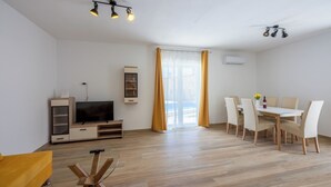A modern living room with a flat-screen TV, a dining table with chairs, and a yellow sofa. - Villa Maluma (Medulin)