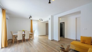 A modern living room with a yellow sofa, a glass coffee table, and a dining area with a table and chairs. - Villa Maluma (Medulin)