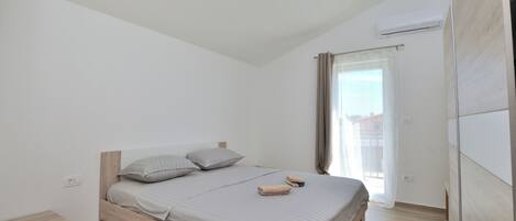 A minimalist bedroom with a wooden bed, a bedside table, and a window with curtains.