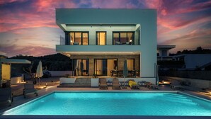 Ein modernes, zweistöckiges Haus mit Swimmingpool, Sitzgelegenheiten im Freien und Blick auf die umliegende Landschaft.