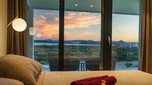 Ein Hotelzimmer mit einem großen Bett, zwei Sesseln, einem kleinen Tisch und Blick auf die Landschaft durch eine Glastür.