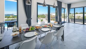 Ein moderner Essbereich mit einem Glastisch, weißen Stühlen und Blick aufs Meer.