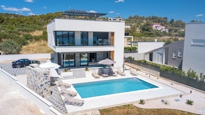 Una moderna casa a due piani con piscina, area relax all'aperto e vista sul paesaggio circostante.