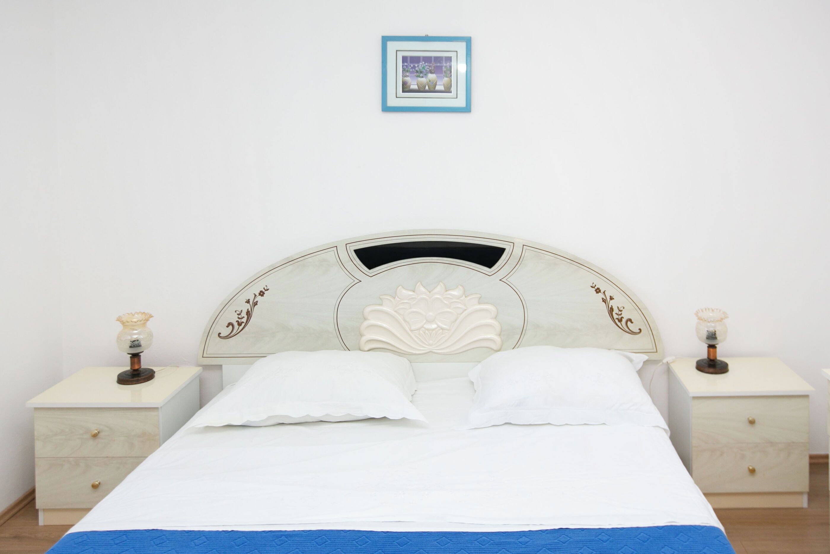 A neatly made bed with white linens and a blue accent at the foot. There are two bedside tables with lamps, one on each side of the bed.