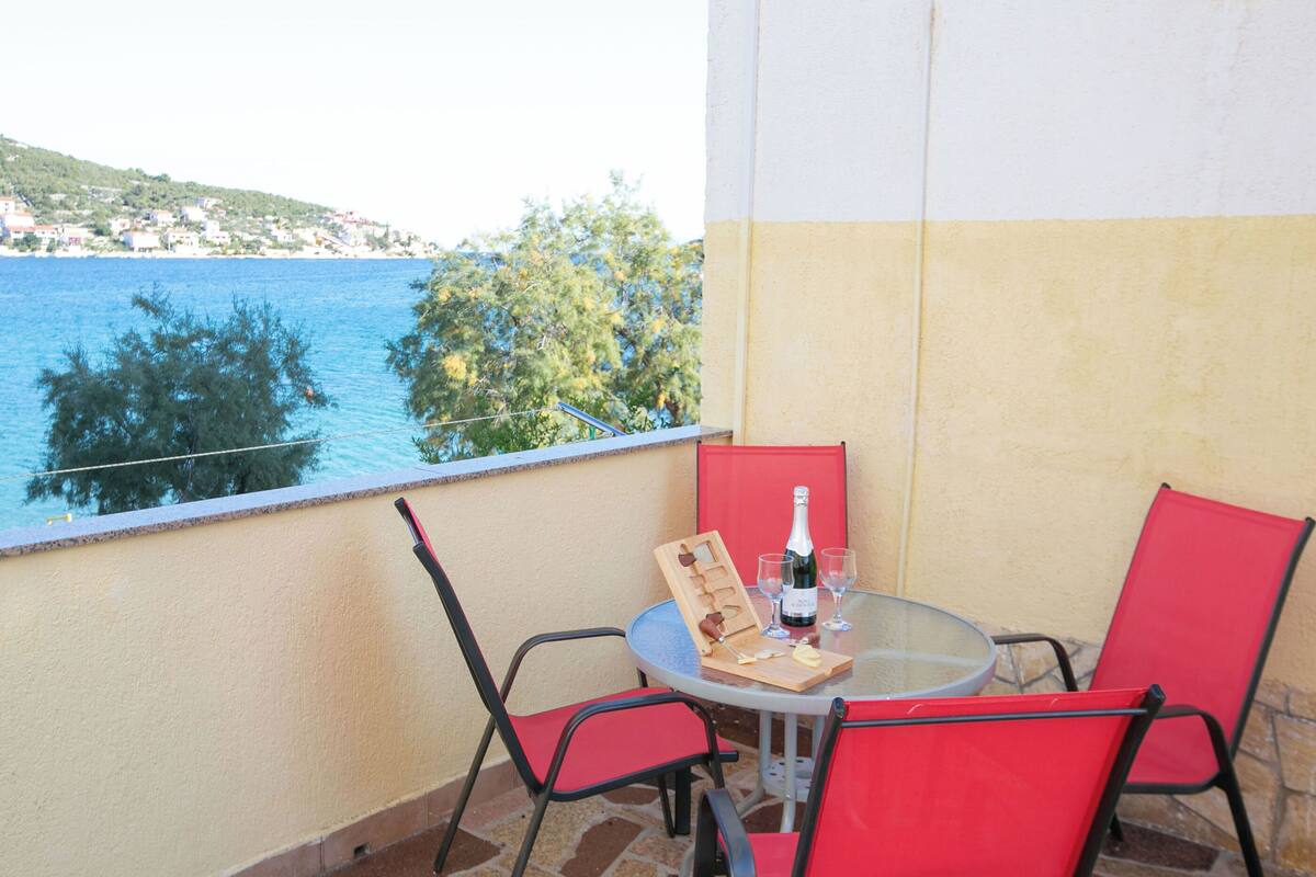 Ένα μπαλκόνι με ένα τραπέζι και καρέκλες, ένα μπουκάλι σαμπάνια και θέα στη θάλασσα και σε μια πόλη που βρίσκεται σε απόσταση.