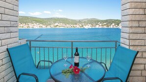 A balcony with a table, two chairs, a bottle of wine, and a flower. - Apartments Tiho II (Marina)