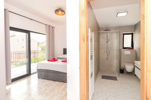 Un dormitorio con cama, puerta corrediza al balcón y baño con ducha e inodoro.
