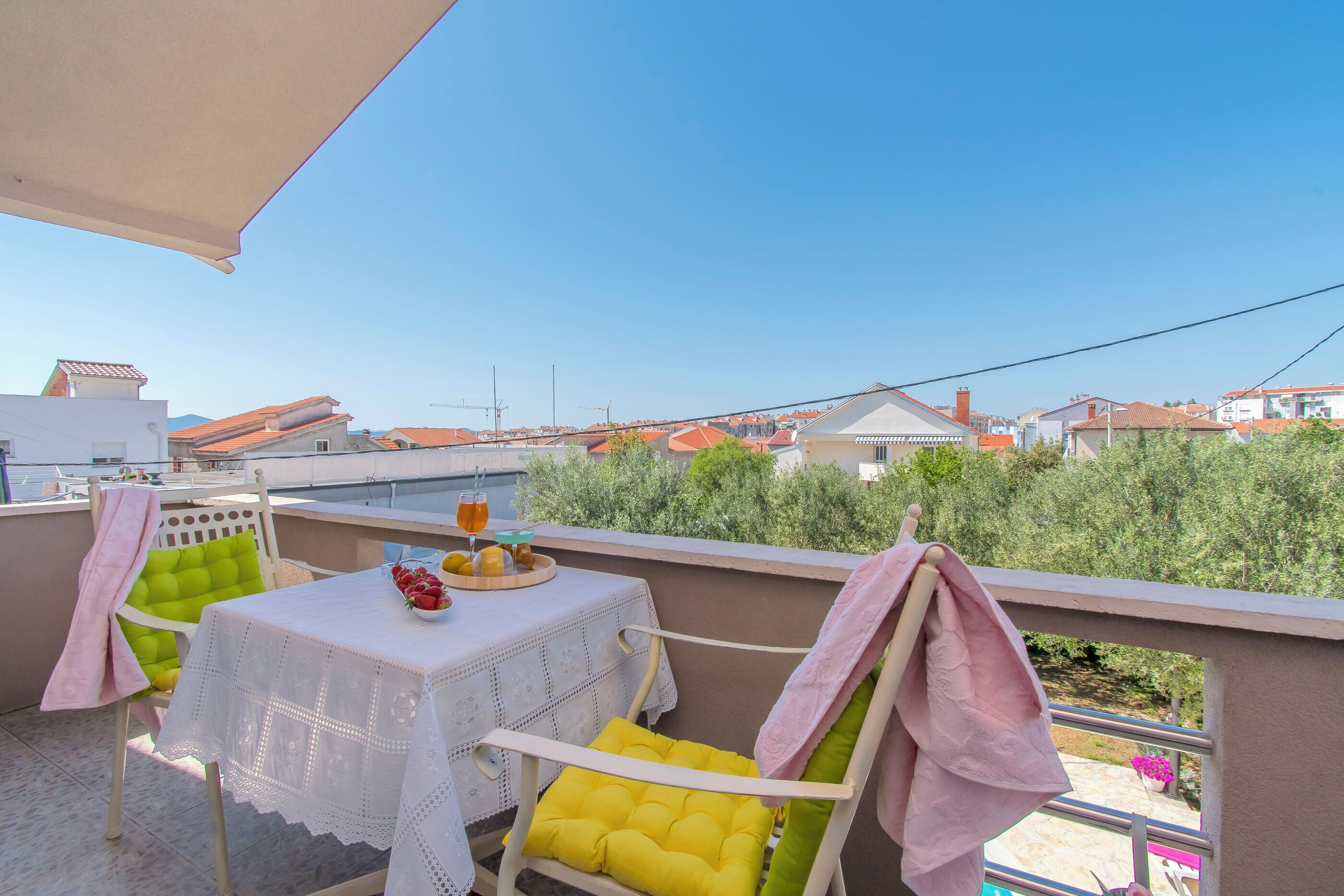 Un balcón con mesa y sillas para dos, con cojines, y vista a una zona residencial.