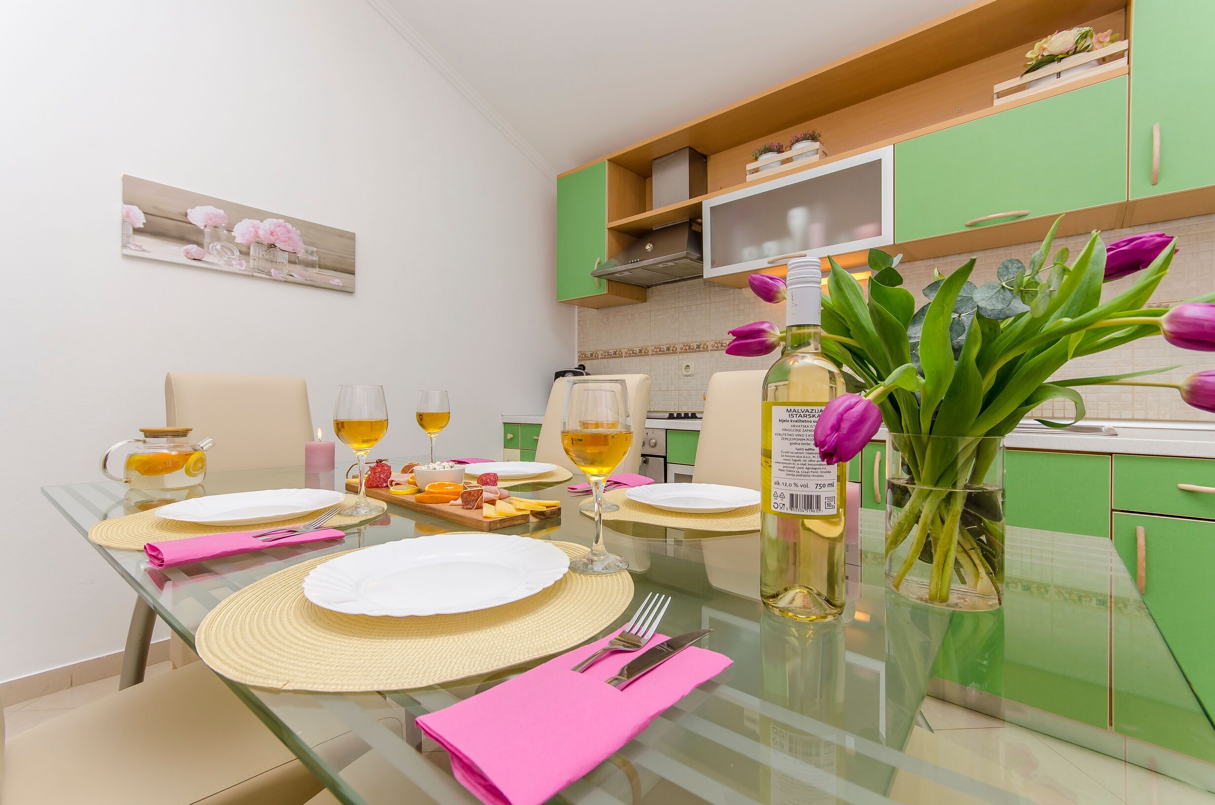 Una mesa de comedor servida con platos, cubiertos y vasos, un florero con flores y una botella de aceite.