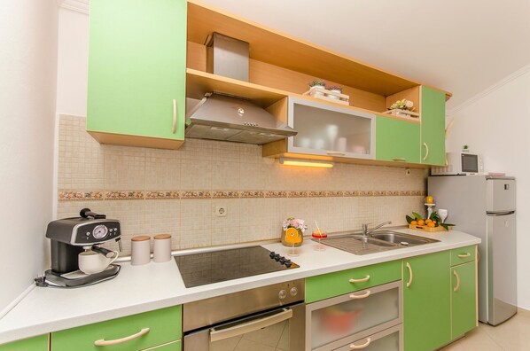 Cucina con mobili verdi, cappa in acciaio inossidabile, forno a microonde integrato e frigorifero.