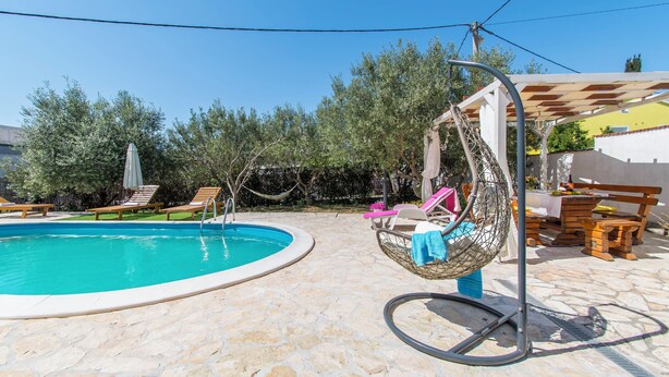 Une piscine avec des chaises longues et un fauteuil suspendu.