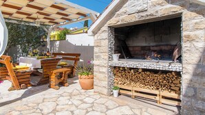 Une terrasse extérieure dotée d’un espace barbecue en pierre, de meubles en bois et d’une pergola.