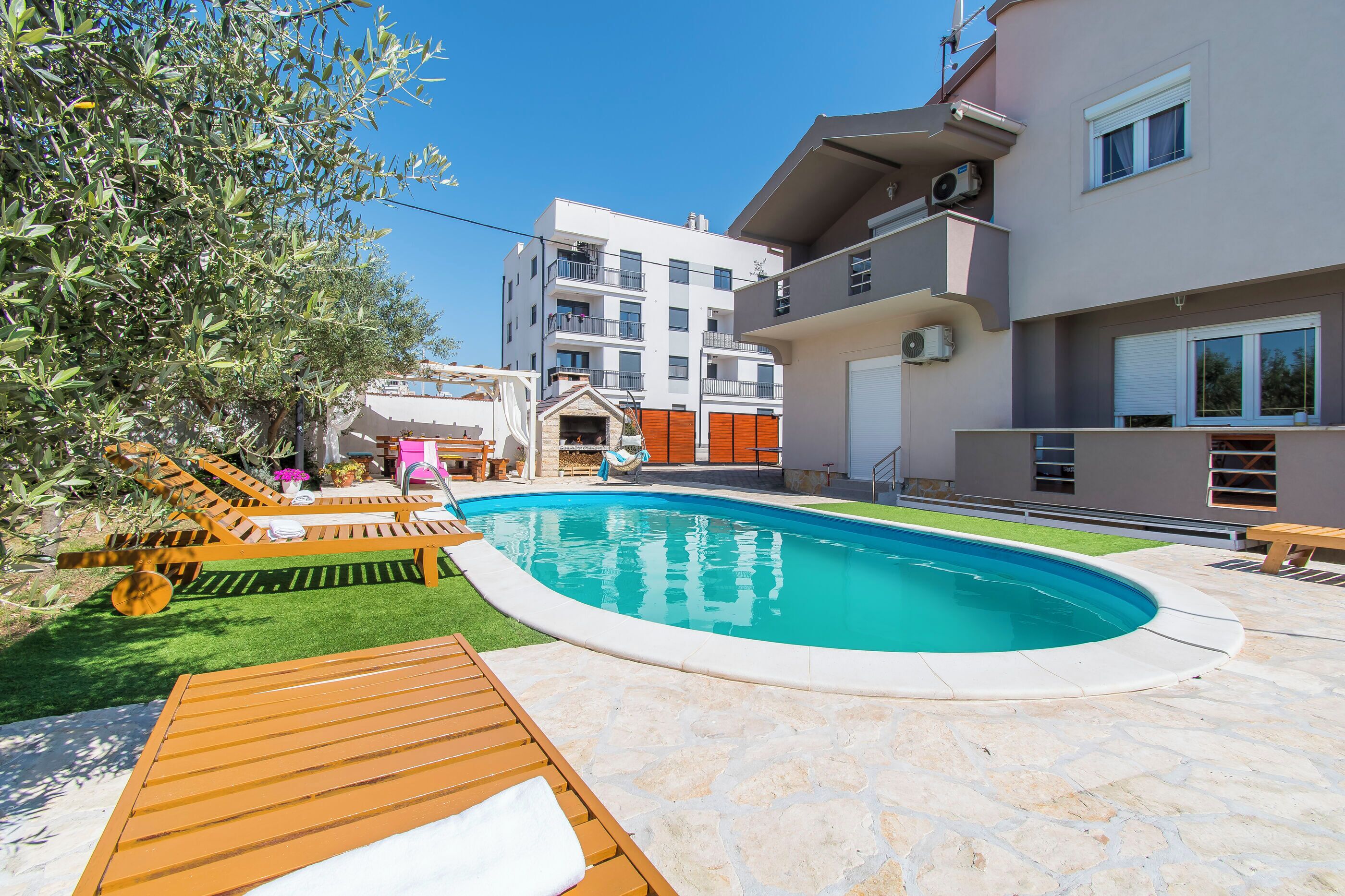 Une piscine avec des chaises longues, une terrasse en pierre et, au fond, un immeuble à plusieurs étages.