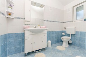 Un bagno con un lavandino bianco, un water e uno specchio sopra il lavandino. Le pareti e il pavimento sono rivestiti di piastrelle blu.