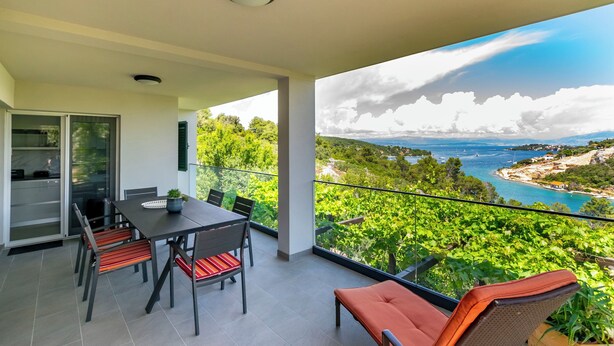 Un balcón con zona de comedor, que incluye una mesa y sillas, con vistas a un paisaje costero con vegetación y el mar.