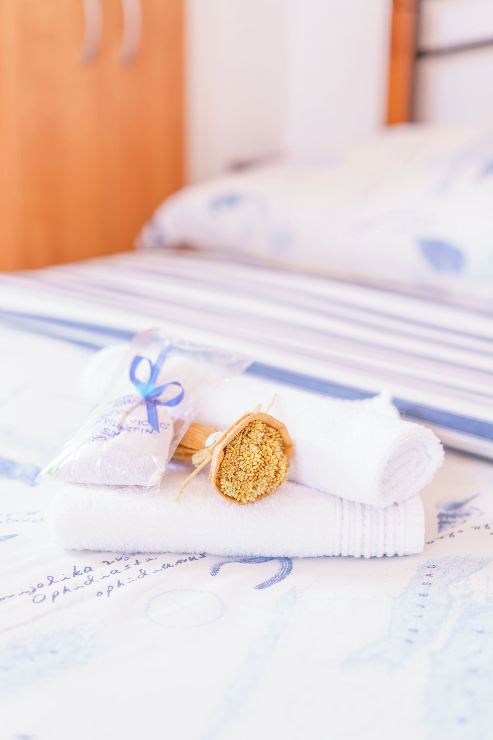 A neatly made bed with a white and blue striped bedspread, a rolled white towel, and a small package tied with a blue ribbon.
