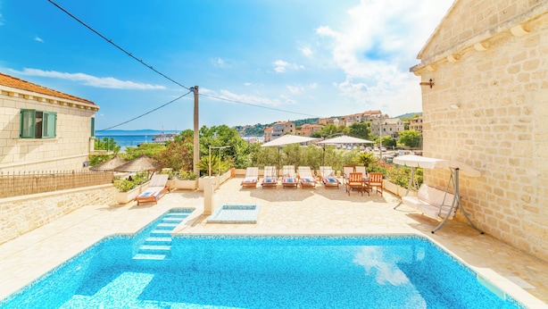 Piscina com espreguiçadeiras e guarda-sóis, com vista para uma cidade costeira.