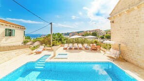 A swimming pool with lounge chairs and umbrellas, overlooking a coastal town.