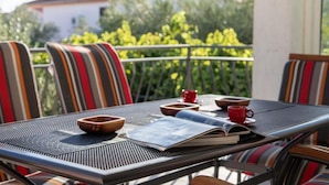 Ein Balkon mit gestreiften Stühlen, einem Tisch mit einer Zeitschrift und einer roten Tasse.