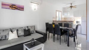 Ein modernes Wohnzimmer mit grauem Sofa, schwarzen Sesseln, einem Esstisch und einer Küche im Hintergrund.