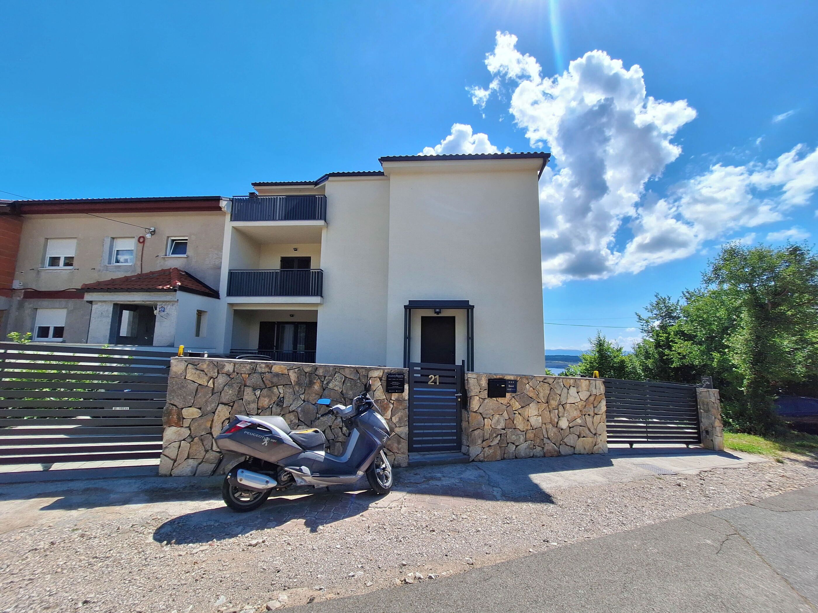 A modern two-story building with a stone wall entrance and a parked scooter.