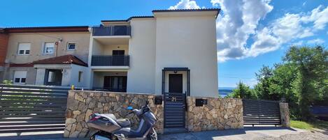 A modern two-story building with a stone wall entrance and a parked scooter.