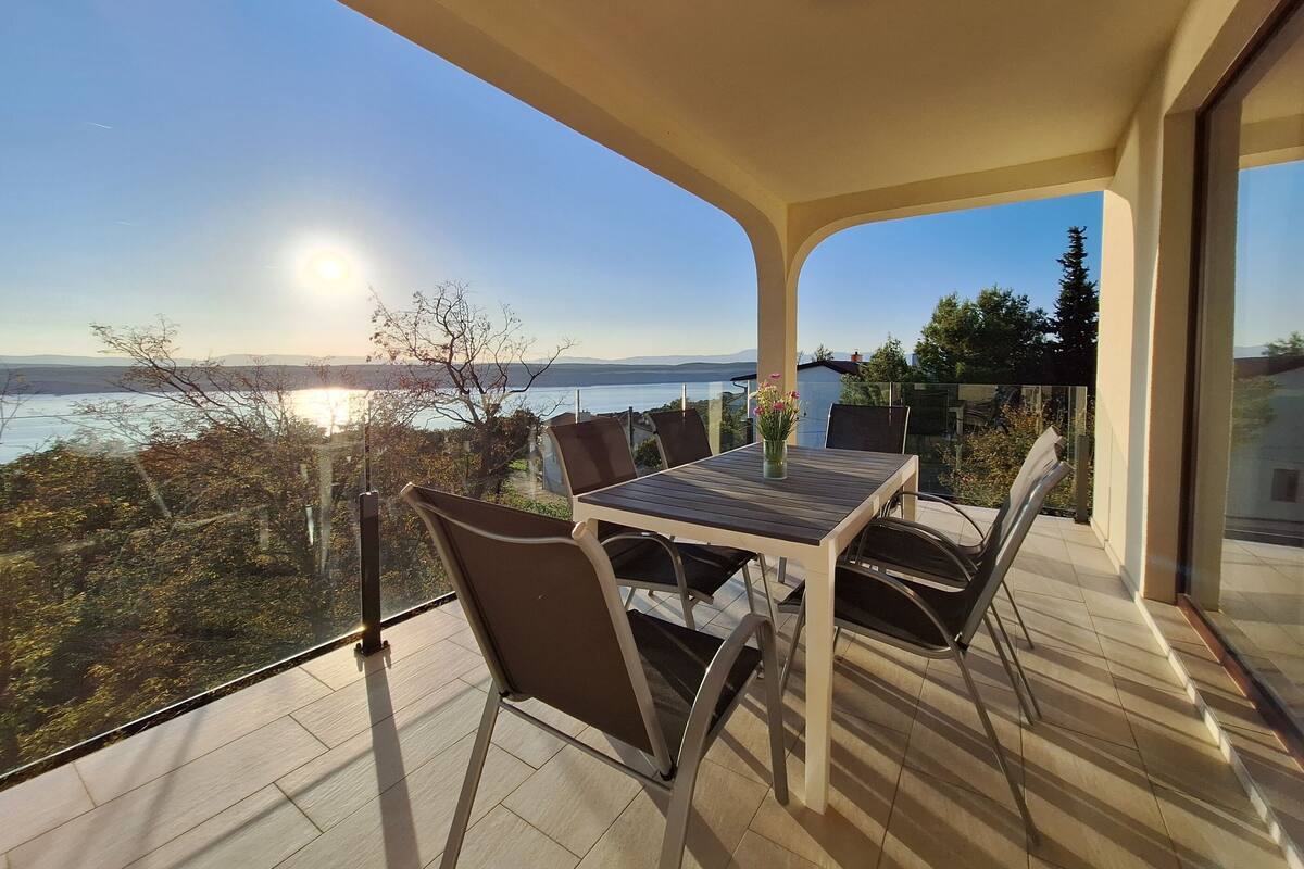 En balkon med et bord og stole, der udover et smukt udsigtspunkt over vand og fjerne bjerge.