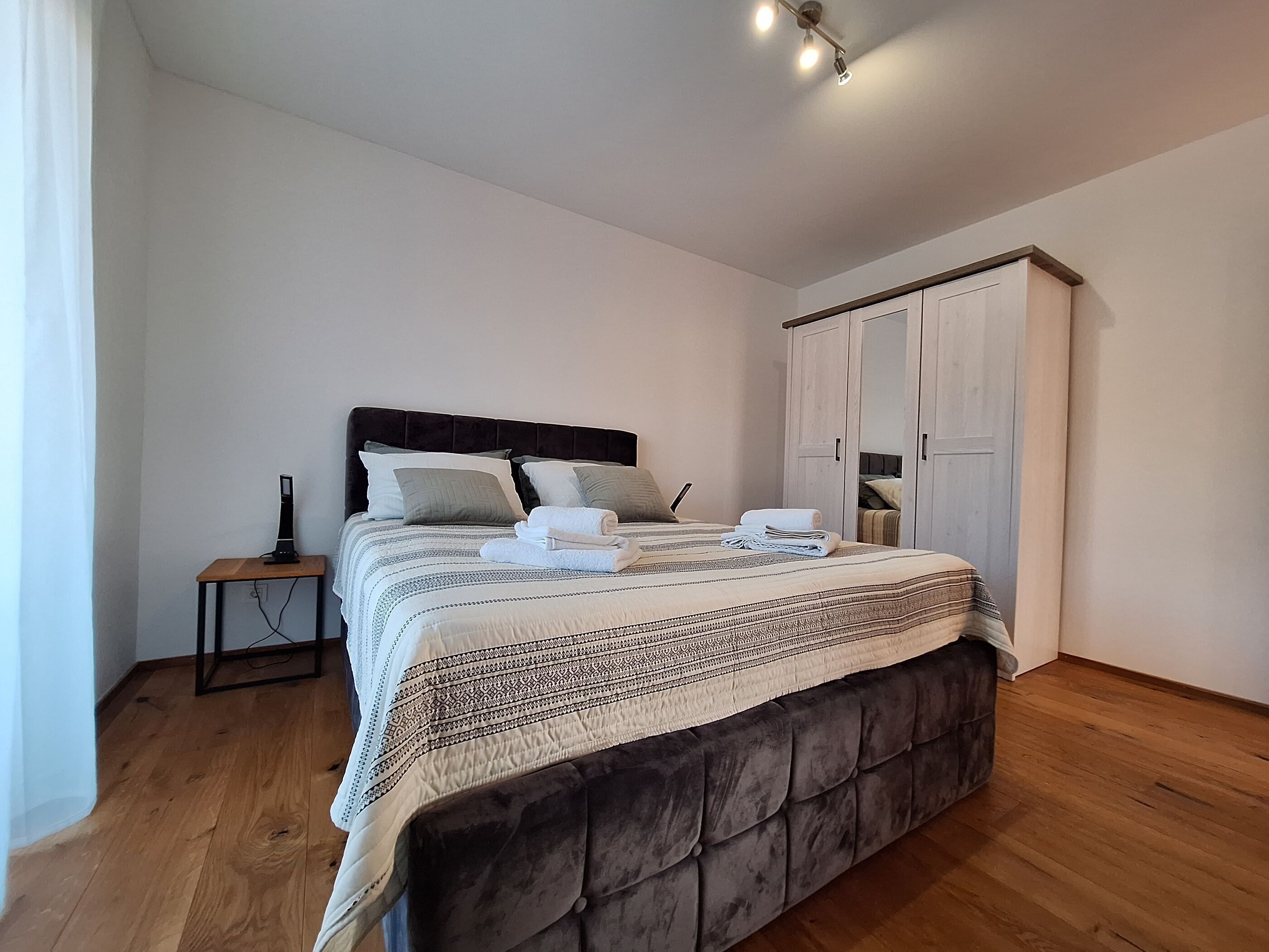 Et soveværelse med en stor seng, et natbord, en garderobe og en loftslampe.