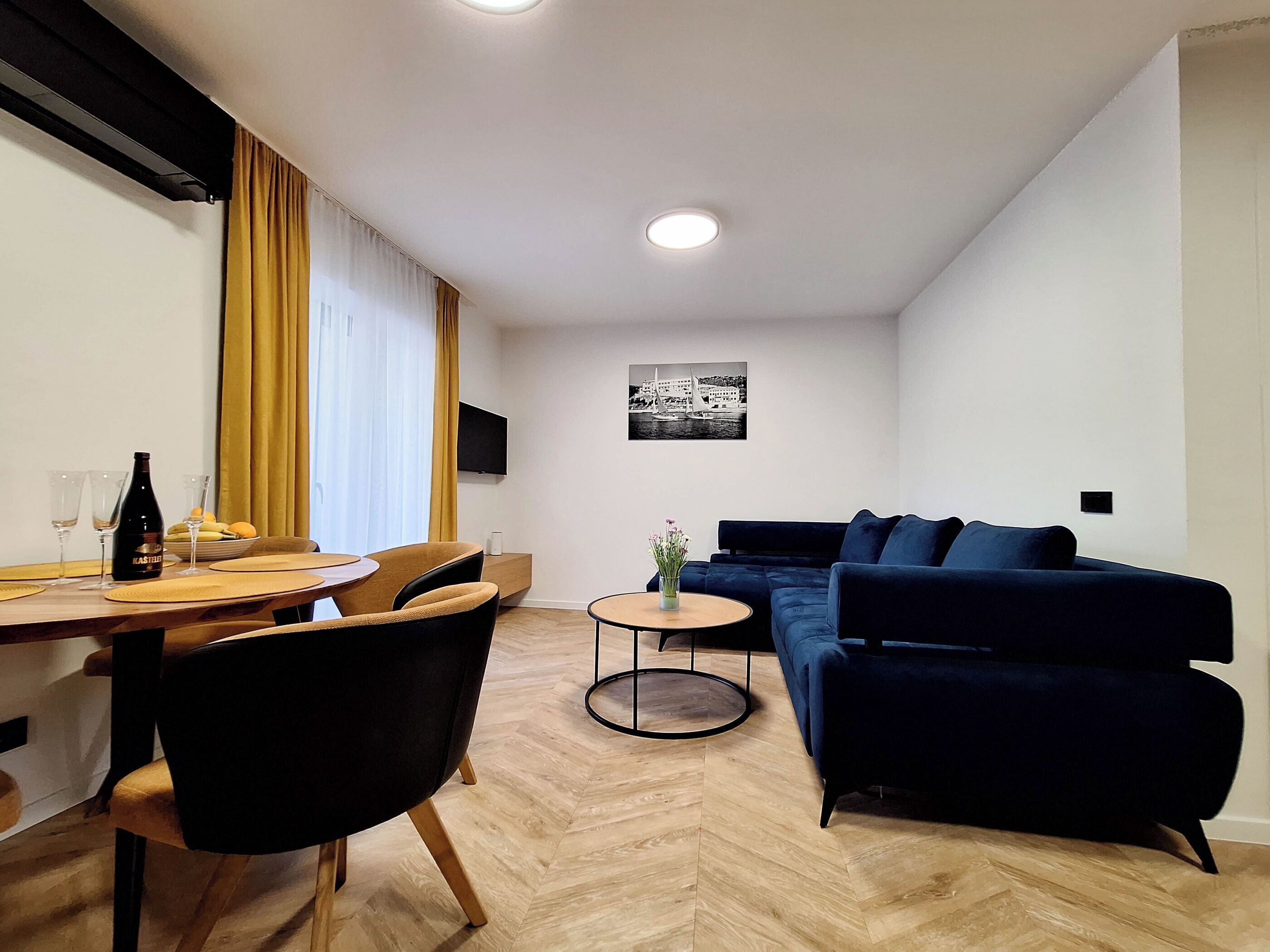 Ett modernt vardagsrum med en matplats, en blå soffa och en platt-TV på väggen.