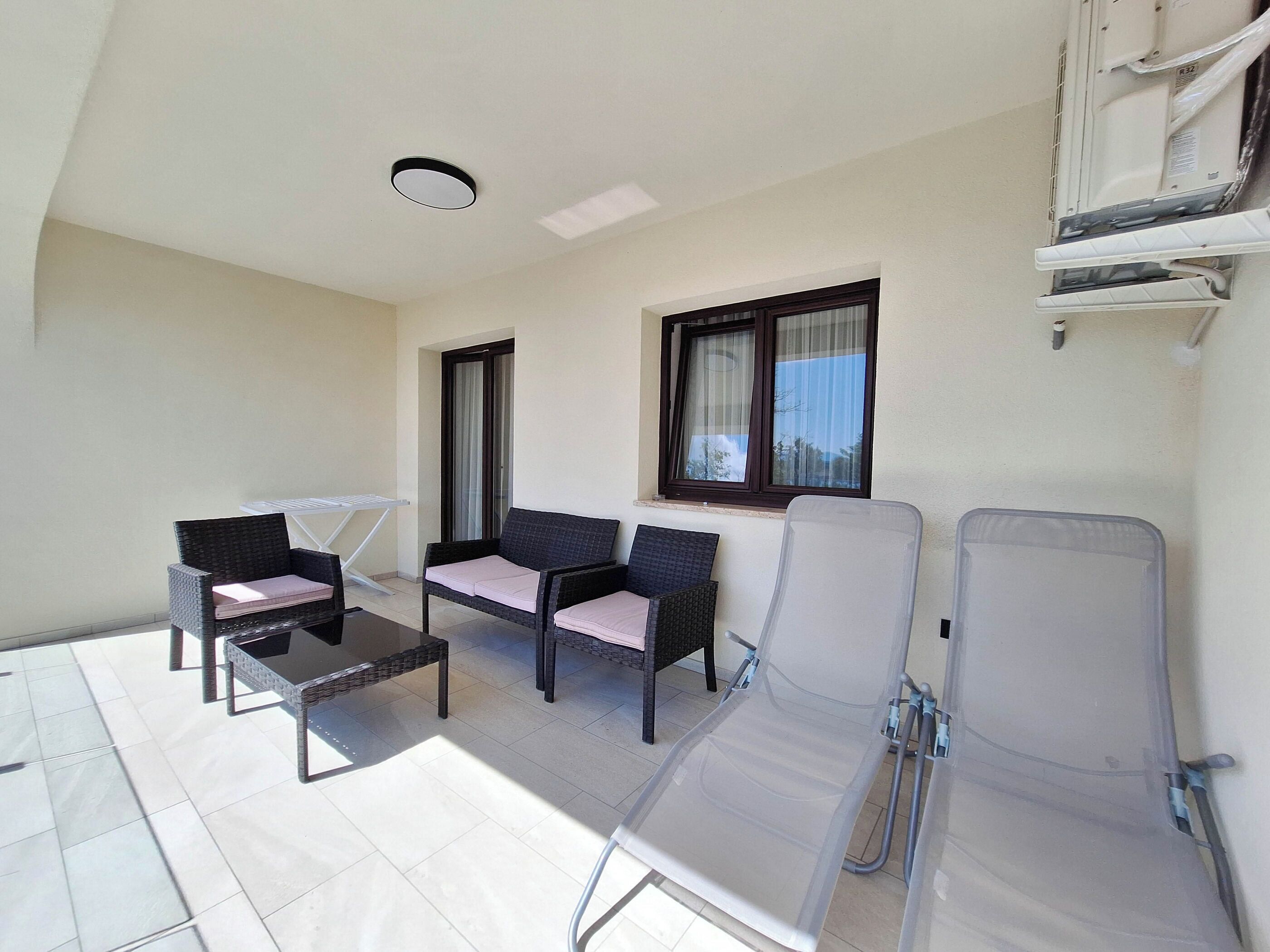 A sunlit balcony with wicker furniture, a small table, and a window with curtains.