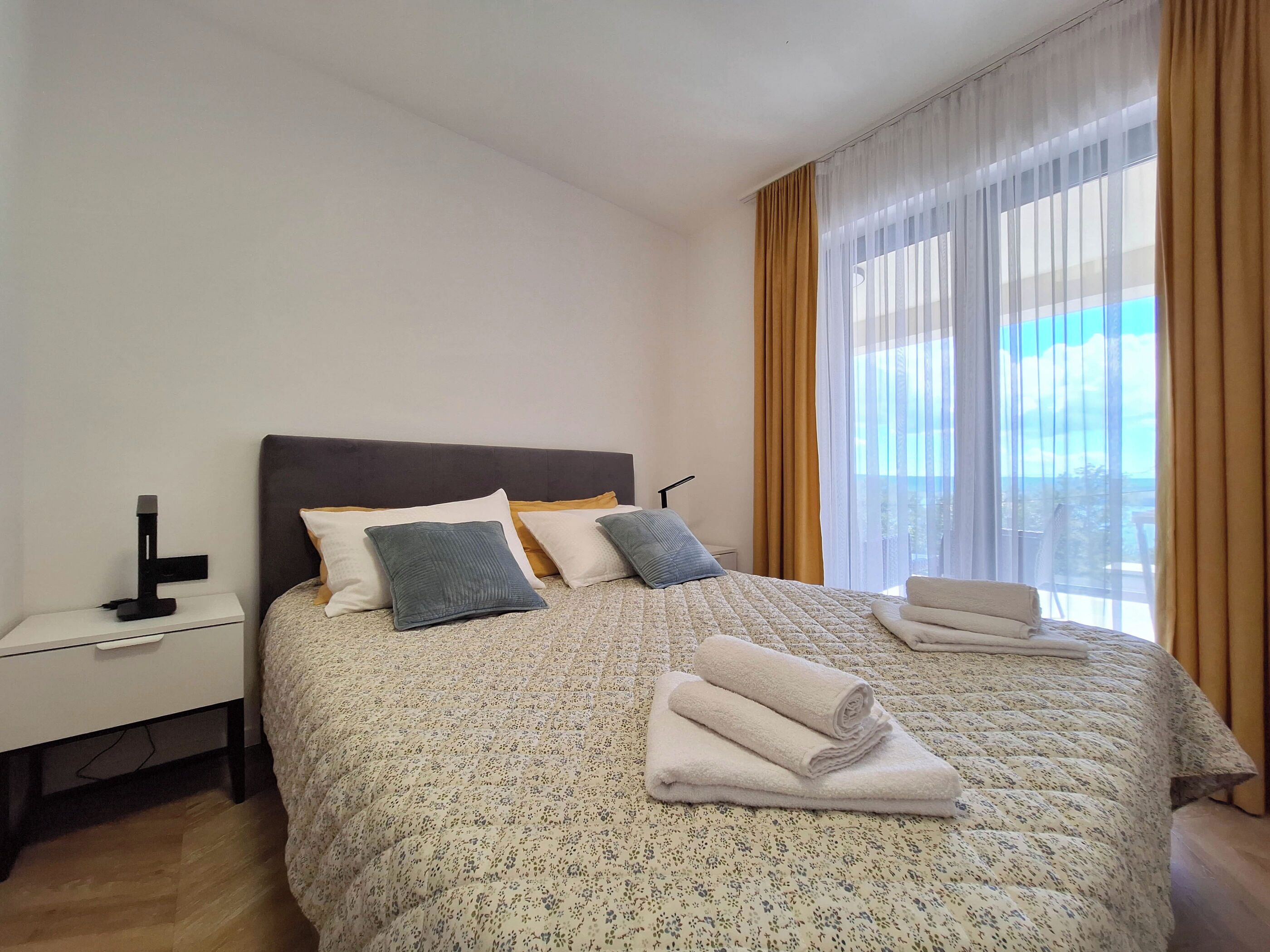 A neatly made bed with a floral-patterned duvet, two pillows, and a folded towel on the side.
