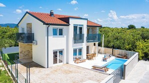 Une maison à deux étages dotée d’une piscine, d’un espace extérieur aménagé et offrant une vue sur la verdure environnante.