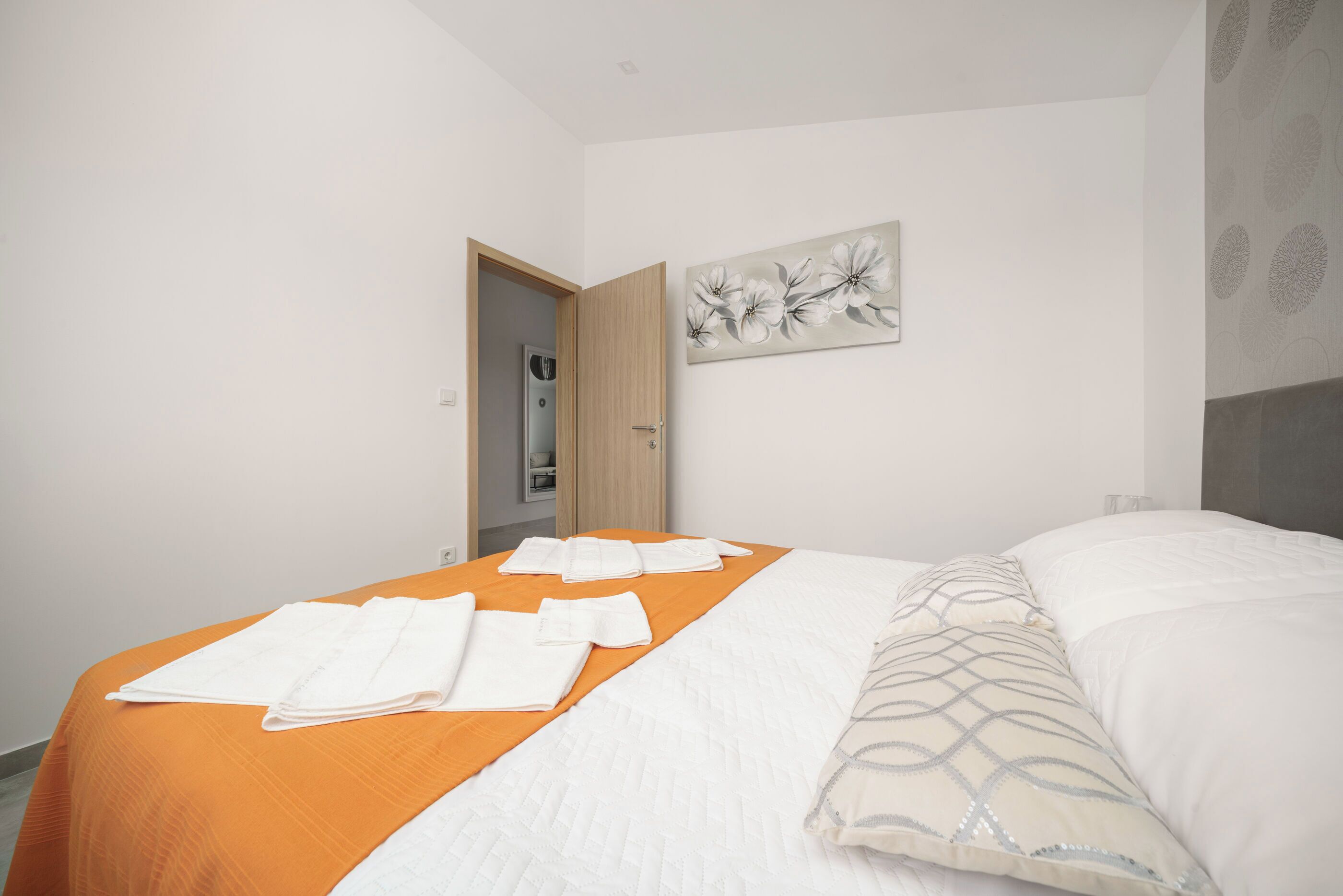 A hotel room with a bed, orange bedspread, white pillows, and a painting on the wall.