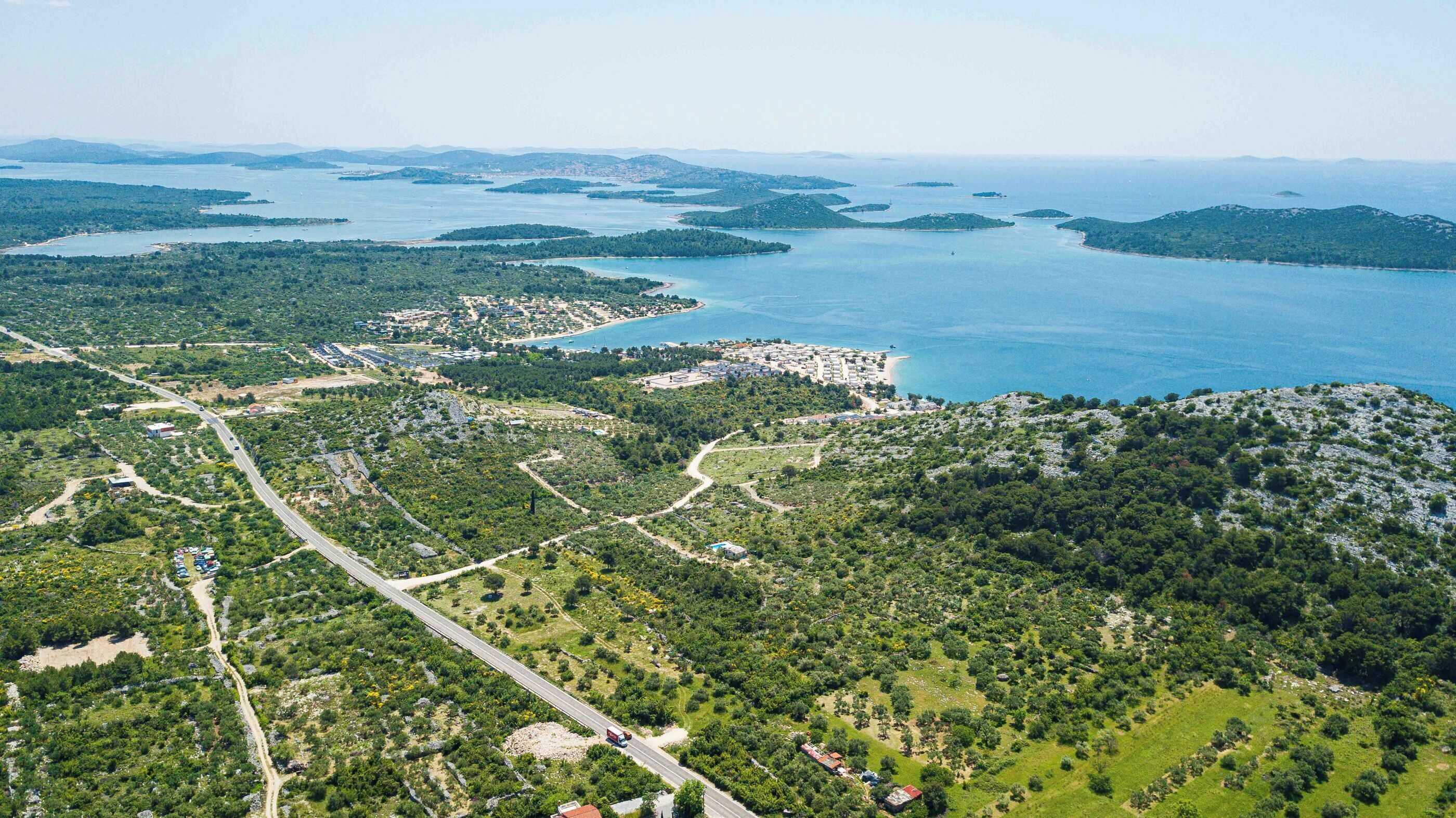 An aerial view of a coastal area with a mix of natural landscapes and developed areas, including roads and buildings.