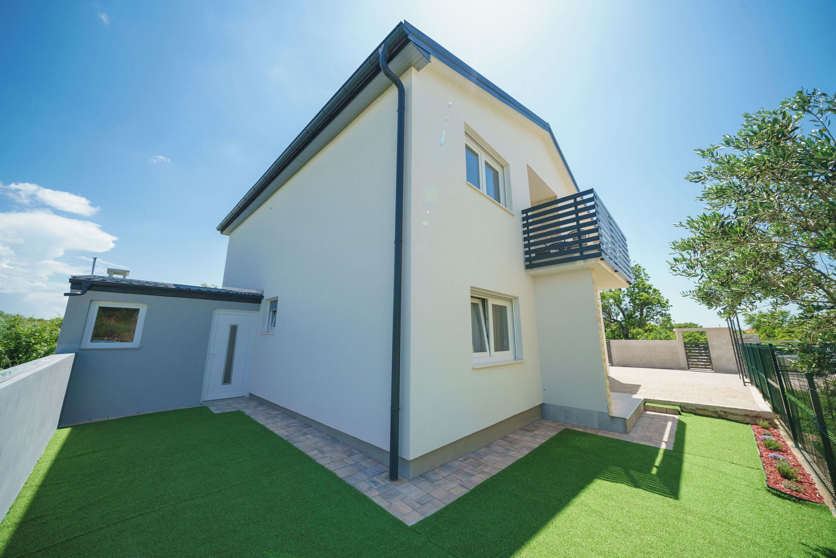 A modern two-story house with a flat roof, a balcony, and a small attached garage.