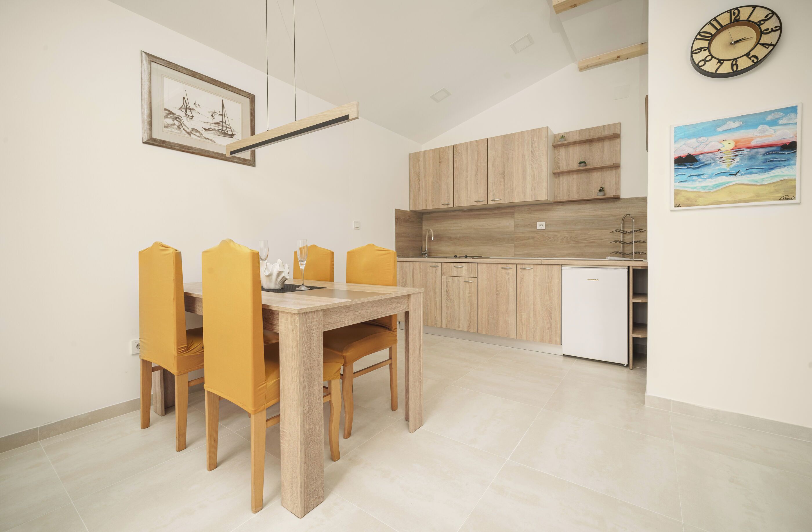Une cuisine moderne avec des meubles en bois, un four encastré et un coin repas comprenant une table et des chaises en bois.