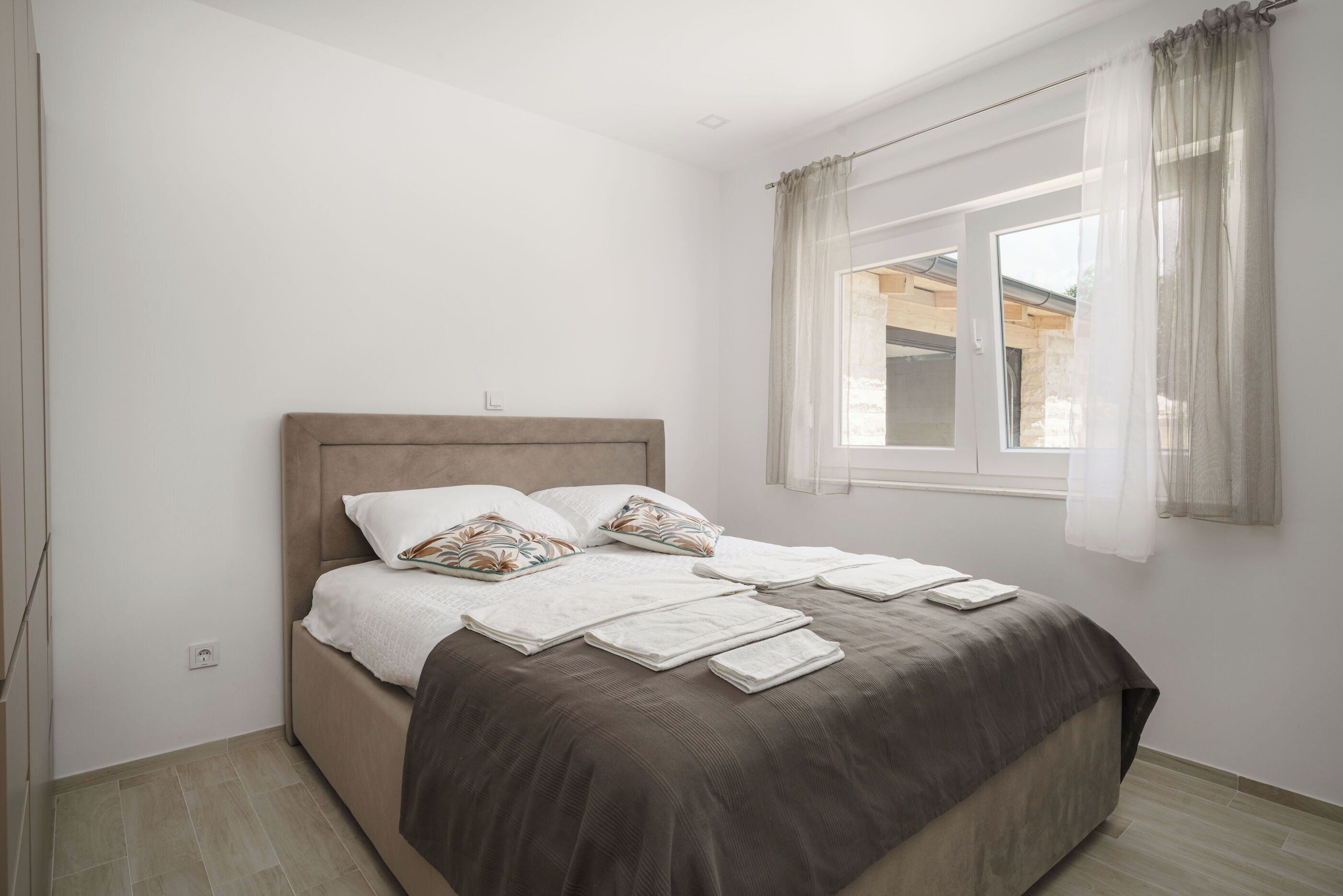 A neatly made bed with a brown headboard, white linens, and decorative pillows.