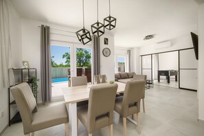 A modern dining area with a wooden table and four chairs, a ceiling light fixture, and a view of the outdoors. - Apartments Fortis (Pakostane)