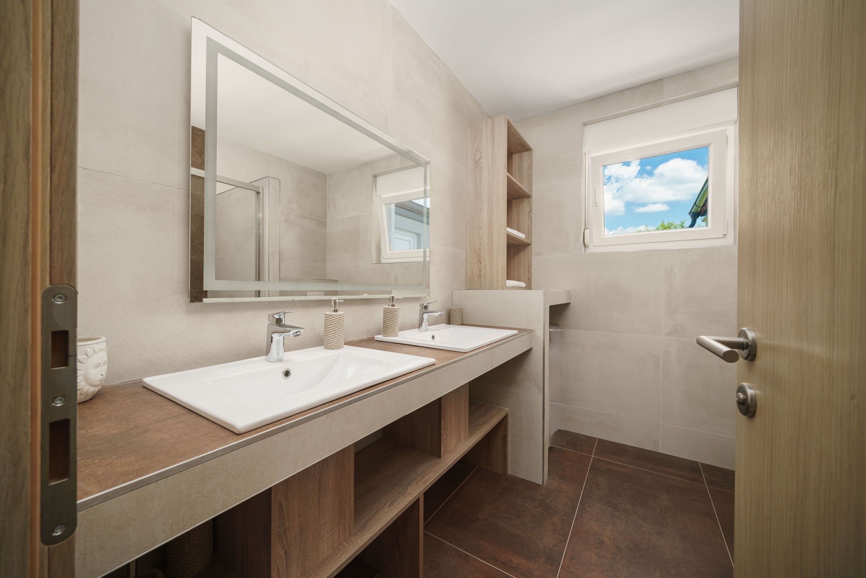 Een moderne badkamer met twee wastafels, een grote spiegel en een raam.