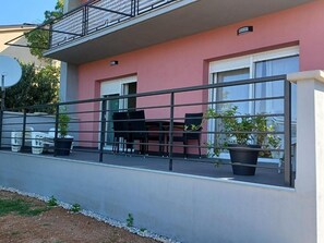A balcony with a metal railing, a table with chairs, and potted plants. - Apartment Snjezana (Senj)