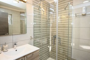 A modern bathroom with a glass shower enclosure, a white sink, and a mirror. - Apartment Snjezana (Senj)