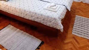 Un lit bien fait, avec une literie à motifs géométriques, un luminaire suspendu et un tapis tissé sur un plancher en bois.