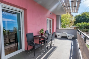 A balcony with a table and chairs, a potted plant, and a view of the street. - Apartment Snjezana (Senj)