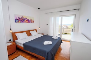 A bedroom with a bed, a nightstand, a dresser, a painting, and a view of the outside. - Apartment Snjezana (Senj)